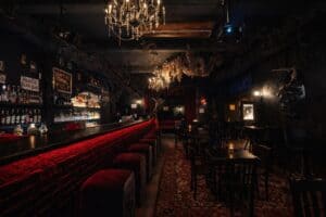 Temný bar s červeně osvětleným pultem lustry a posezením v gotickém stylu