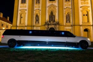 Bílá limuzína Lincoln s modrým LED osvětlením zaparkovaná večer před historickým kostelem v Olomouci
